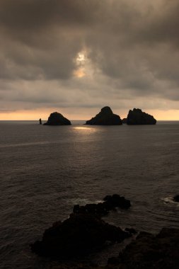 Okyanustaki küçük kayalık adalarının gün batımı manzarası ve güneş bulutları delip geçiyor. Heimaey Adası, Vestmannaeyjar, İzlanda.