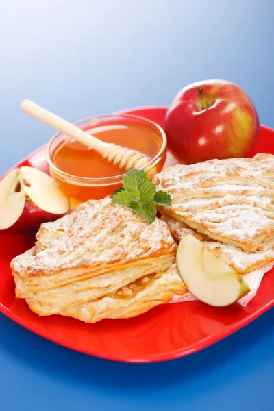 Pasteles de manzana en el plato, miel y trozos de manzana alrededor — Foto de Stock