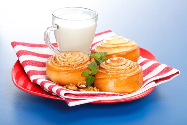 Three cinnamon rolls and jug of milk on red plate — Stock Photo, Image