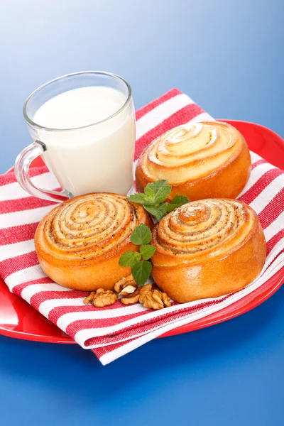 Three cinnamon rolls and jug of milk on red plate — Stock Photo, Image