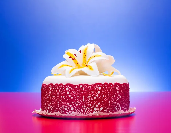 Λευκό φοντάν κέικ διακοσμημένο με κόκκινη δαντέλα και βρώσιμα καραμέλα κρίνος — Φωτογραφία Αρχείου