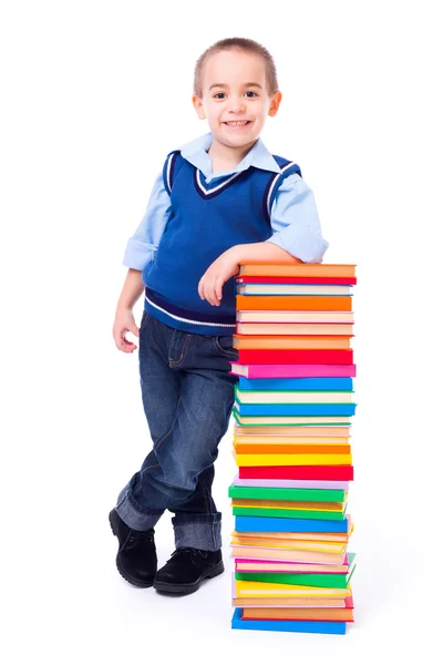 Маленький мальчик стоит рядом со стопкой красочных книг — стоковое фото
