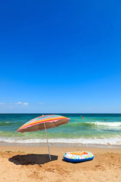 Beach umbrella and toy boat at sea — Stock Photo, Image