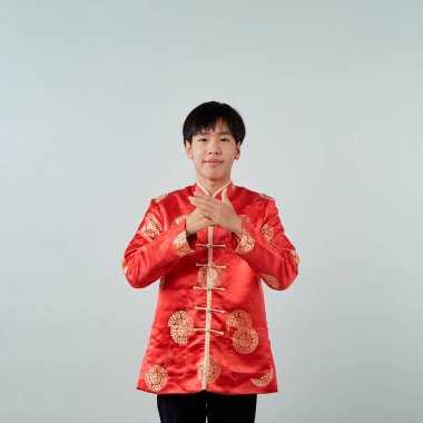 Kırmızı mandalina yakalı genç bir Asyalı stüdyo gri arka planda bir tebrik jesti sergiliyor Mutlu Çin Yeni Yılı