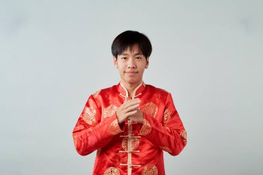 Kırmızı mandalina yakalı genç bir Asyalı stüdyo gri arka planda bir tebrik jesti sergiliyor Mutlu Çin Yeni Yılı