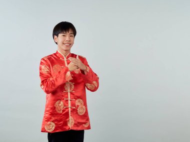 Kırmızı mandalina yakalı genç bir Asyalı stüdyo gri arka planda bir tebrik jesti sergiliyor Mutlu Çin Yeni Yılı