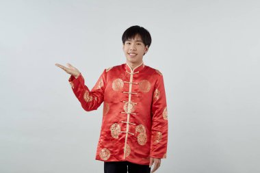 Mutlu Asyalı adam geleneksel oryantal kostüm. Yeni yıl Çin kavramları için izole edilmiş gri arka planda ürünün fotokopi alanı ile avuçlarını açık gösteriyor.