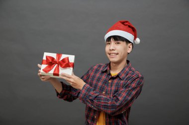 Noel partisi ve tatil konsepti. Genç Asyalı adam, gri arka planda izole edilmiş, hediye kutusu stüdyosu fotoğrafı tutuyor.