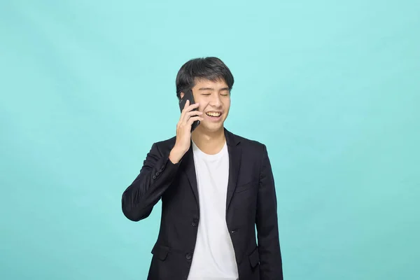 Młody Uśmiechnięty Przystojny Azjata Garniturze Mówi Przez Telefon Jasnoniebieski Odizolowane — Zdjęcie stockowe