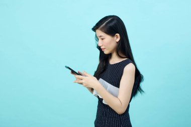 Asyalı genç bayanın cep telefonunu olumlu bir ifadeyle kullanmasına, geniş bir şekilde gülümsemesine, günlük kıyafetler giymesine ve mavi arka plandaki kameraya bakmasına şaşırdım. Mutlu, mutlu, mutlu kadın başarıya sevinir..