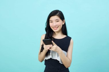 Asyalı genç bayanın cep telefonunu olumlu bir ifadeyle kullanmasına, geniş bir şekilde gülümsemesine, günlük kıyafetler giymesine ve mavi arka plandaki kameraya bakmasına şaşırdım. Mutlu, mutlu, mutlu kadın başarıya sevinir..