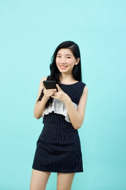 Asyalı genç bayanın cep telefonunu olumlu bir ifadeyle kullanmasına, geniş bir şekilde gülümsemesine, günlük kıyafetler giymesine ve mavi arka plandaki kameraya bakmasına şaşırdım. Mutlu, mutlu, mutlu kadın başarıya sevinir..