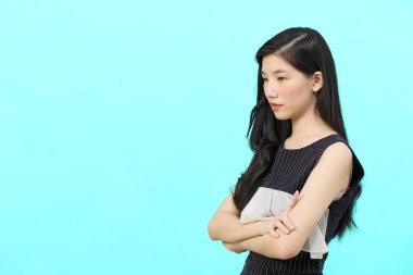 Asyalı iş kadını iktidarda duruyor. Profesyonel iş adamı göğsünde çapraz silahlar, mavi arka planda duruyor.