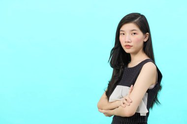 Asyalı iş kadını iktidarda duruyor. Profesyonel iş adamı göğsünde çapraz silahlar, mavi arka planda duruyor.