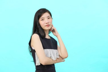 Asyalı iş kadını iktidarda duruyor. Profesyonel iş adamı göğsünde çapraz silahlar, mavi arka planda duruyor.