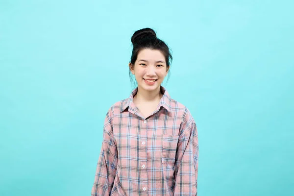可爱的亚洲女孩笑着穿着宽松的格子呢衬衫站着 在蓝色的背景下感到快乐和自信 — 图库照片