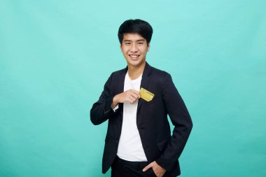 Mavi bir stüdyoda izole edilmiş sarı kredi kartı taşıyan takım elbiseli yakışıklı bir iş adamı portresi