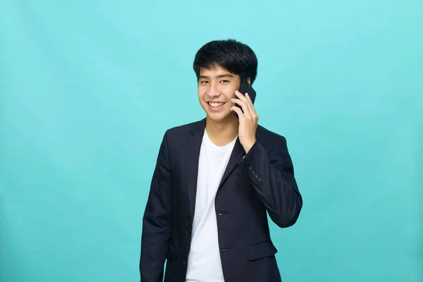 一个身穿半正式西服 面带微笑的年轻英俊亚洲男子的画像 他用的是一部背景为浅蓝色 与外界隔绝的手机 — 图库照片
