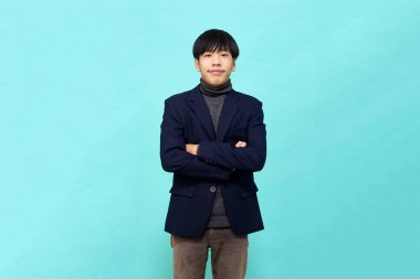 Genç Güneydoğu Asyalı, mutlu ve kendine güveni tam, hafif mavi stüdyoda çapraz kollu, kendine güvenen bir adam.