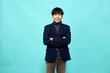 Genç Güneydoğu Asyalı, mutlu ve kendine güveni tam, hafif mavi stüdyoda çapraz kollu, kendine güvenen bir adam.