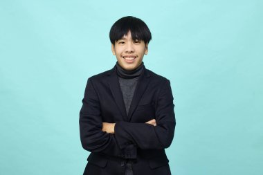 Genç Güneydoğu Asyalı, mutlu ve kendine güveni tam, hafif mavi stüdyoda çapraz kollu, kendine güvenen bir adam.