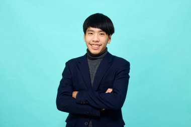 Genç Güneydoğu Asyalı, mutlu ve kendine güveni tam, hafif mavi stüdyoda çapraz kollu, kendine güvenen bir adam.