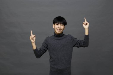 Genç yakışıklı Asyalı adam gri izole arkaplanda yer kopyalamak için poz veriyor.