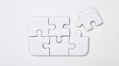 Beyaz arkaplanda dört beyaz yapboz parçası var. Beş tanesi zaten birleştirilmiş. Birleştirmek için bir parçası eksik.