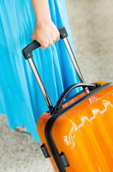 Mujer en vestido azul sostiene maleta naranja en la mano — Foto de Stock