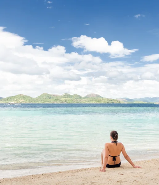 Unga vackra kvinnan sitter på sanden vid havet — Stockfoto