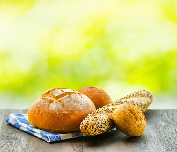 Fresh bread and checkered napkin on wooden table on rural backgr — Stock Photo, Image