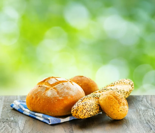 Fresh bread and checkered napkin on wooden table on rural backgr — Stock Photo, Image