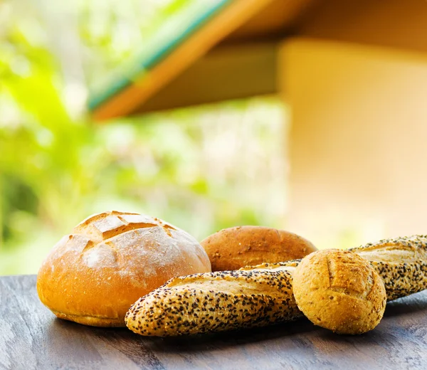 Fresh bread on black wooden table on rural landscape background — Stock Photo, Image