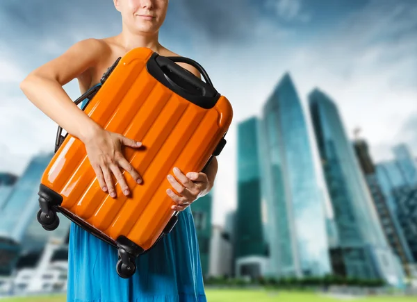 Kobieta w niebieska sukienka posiada walizce pomarańczowy w ręce — Zdjęcie stockowe