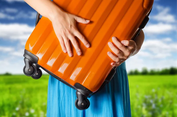 Vrouw in blauwe jurk houdt oranje koffer in handen op het veld — Stockfoto