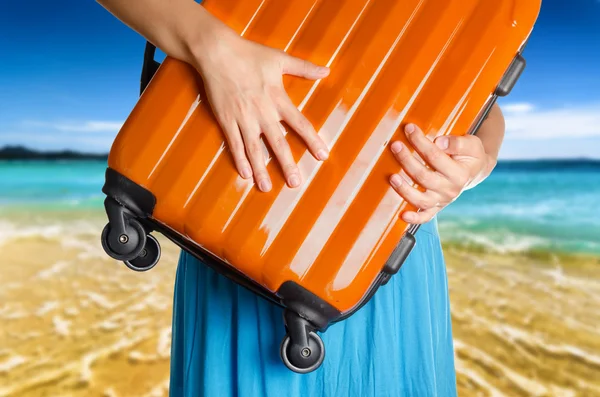 Mujer en vestido azul sostiene maleta naranja en las manos en la playa — Foto de Stock