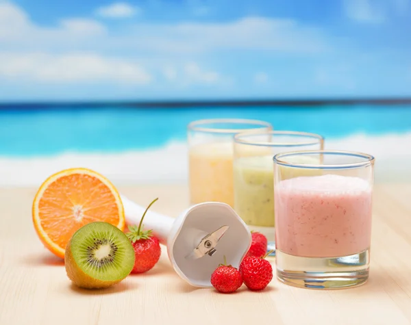 Fruit smoothie on wooden table on tropical beach — Stock Photo, Image