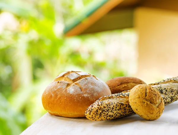 Fresh bread on white wooden table on rural landscape background — Stock Photo, Image