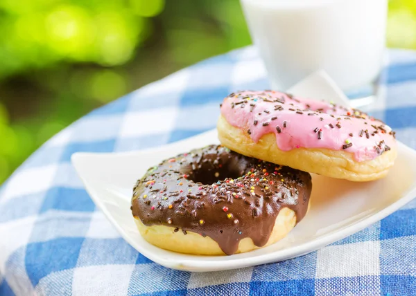 Ciambelle fresche e bicchiere di latte su sfondo naturale — Foto Stock