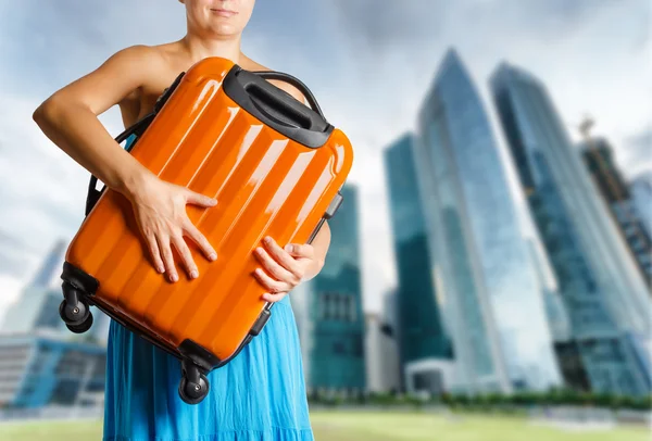 Vrouw in blauwe jurk houdt oranje koffer in handen — Stockfoto