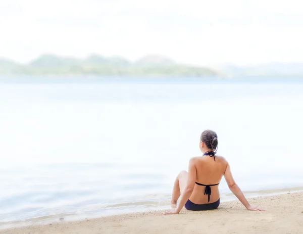 Jovem mulher bonita está sentada na areia junto ao mar — Fotografia de Stock