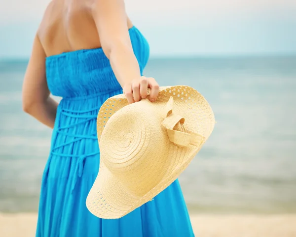 Kobieta w niebieska sukienka wyrzuca kapelusz na plaży — Zdjęcie stockowe