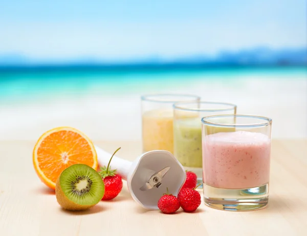 Fruit smoothie on wooden table on tropical beach — Stock Photo, Image