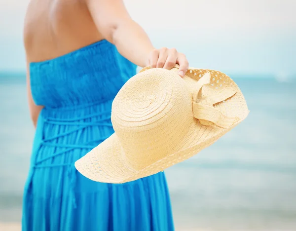 Vrouw in blauwe jurk gooit hoed op het strand — Stockfoto