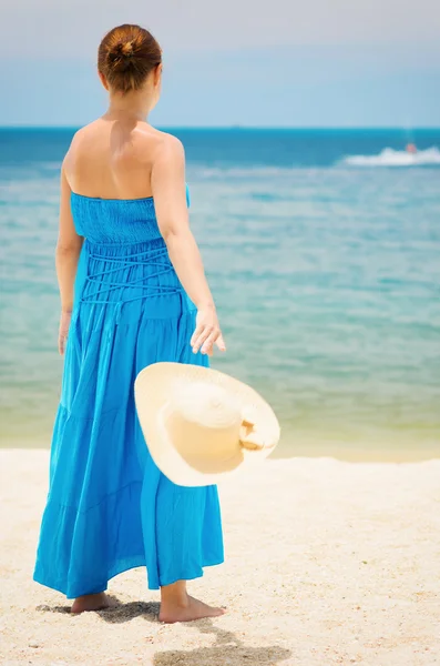 Donna in abito blu lancia cappello sulla spiaggia — Foto Stock