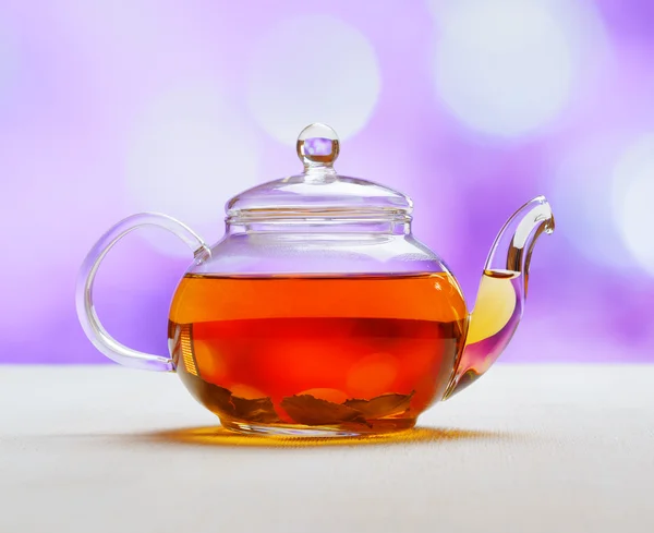 Teapot of fresh tea on purple background — Stock Photo, Image