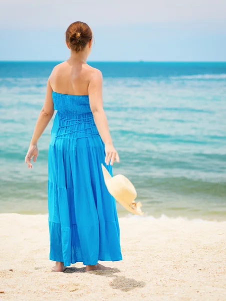 Žena v modrých šatech hází klobouk na pláži — Stock fotografie
