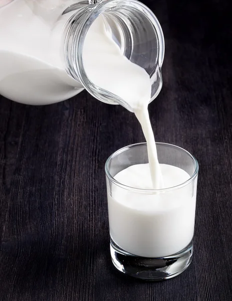 Milch in ein Glas auf schwarzer Tafel gießen — Stockfoto