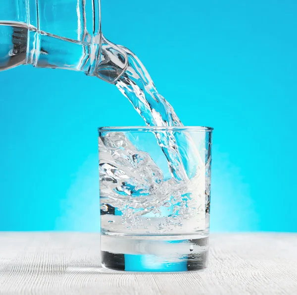 Wasser gießt in ein Glas auf blauem Hintergrund — Stockfoto