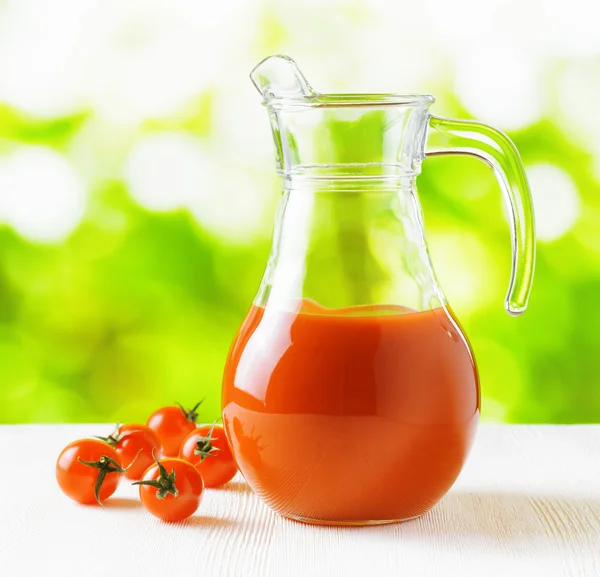 Jug of tomato juice on nature background. Half full pitcher — Stock Photo, Image